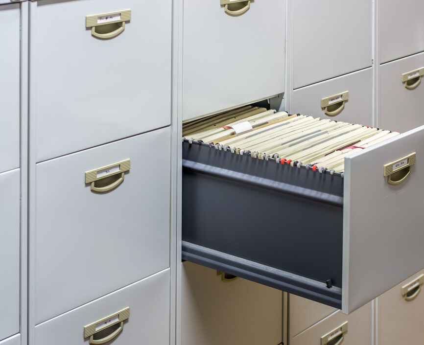 A wall of file cabinet drawers with one open filled with file folders