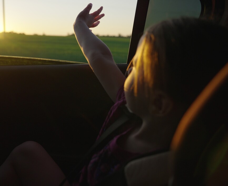 Young girl looks out car window at field