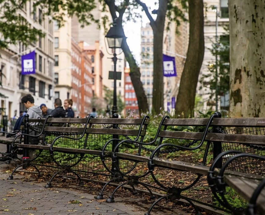 Park benches in Washington Square Park with NYU flags in the background