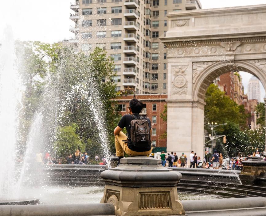 Student sitting near fountain in front of Washington Square Arch