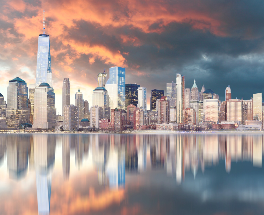 skyline view of manhattan with reflection in water, with fiery orange sunlight shining on clouds