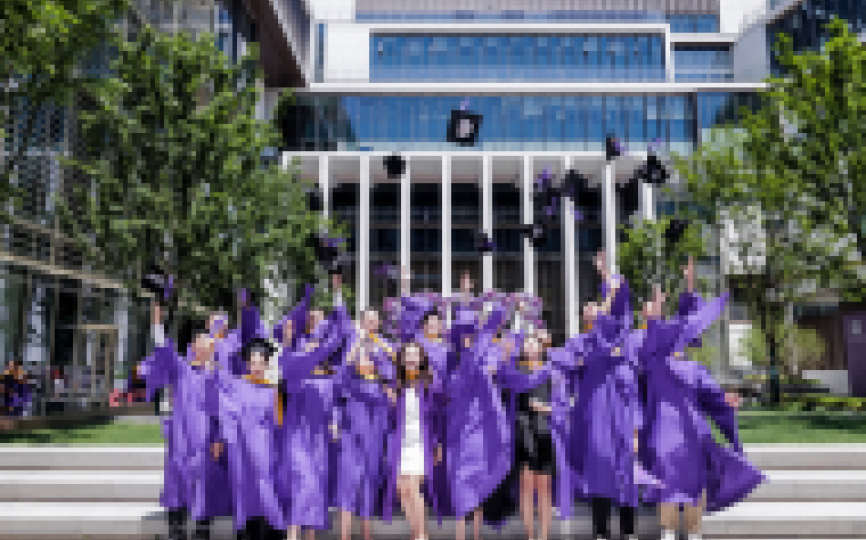Students in violet graduation attire throwing their caps in the air. 