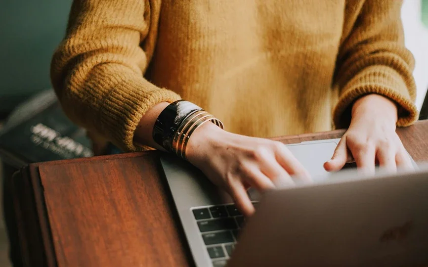Person in a yellow sweater using a laptop.