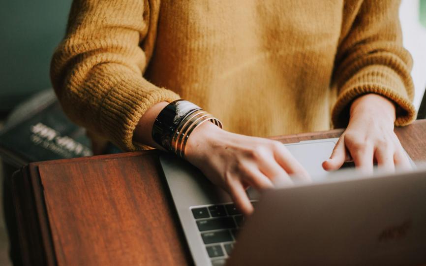 Person in a yellow sweater using a laptop.