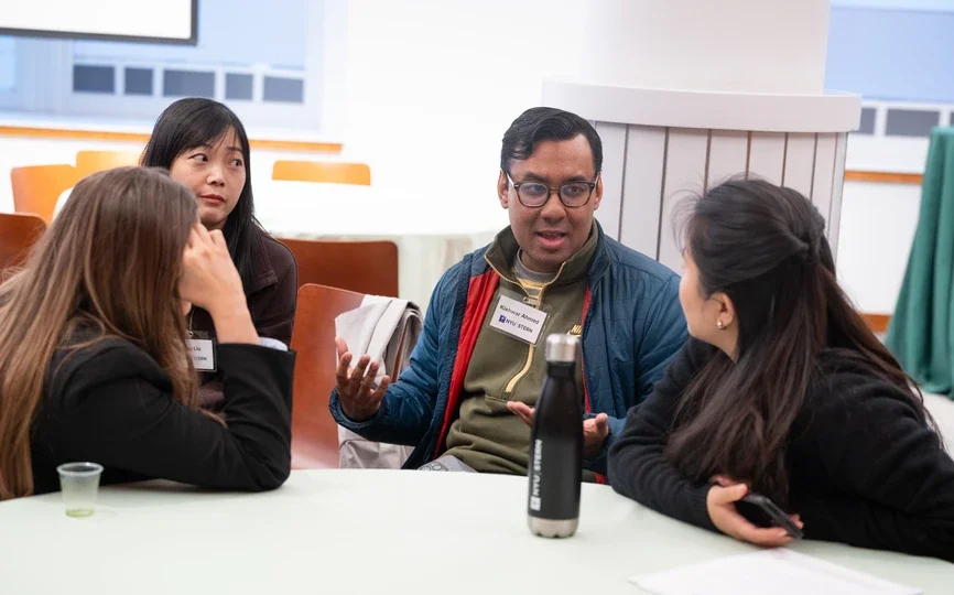 A group of four students chats around a table.