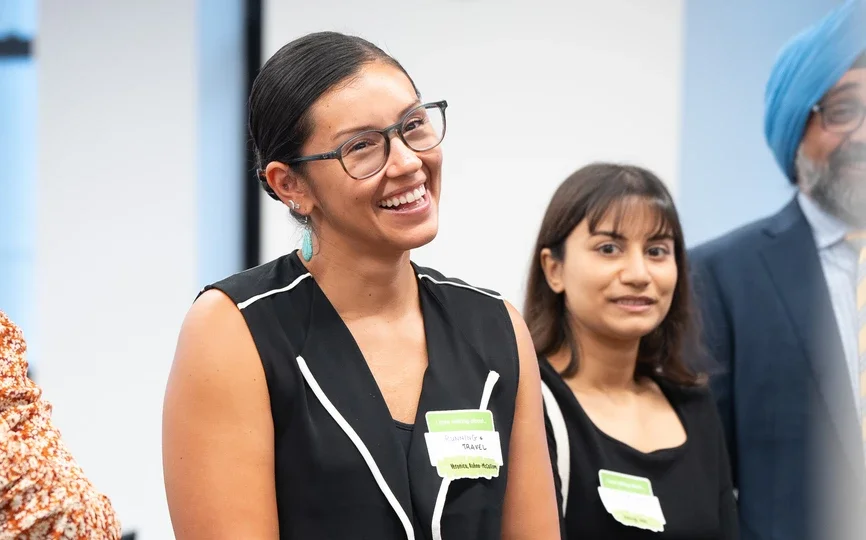 A feminine-presenting person with black hair pulled into a bun smiles while holding her hands across her lower body.