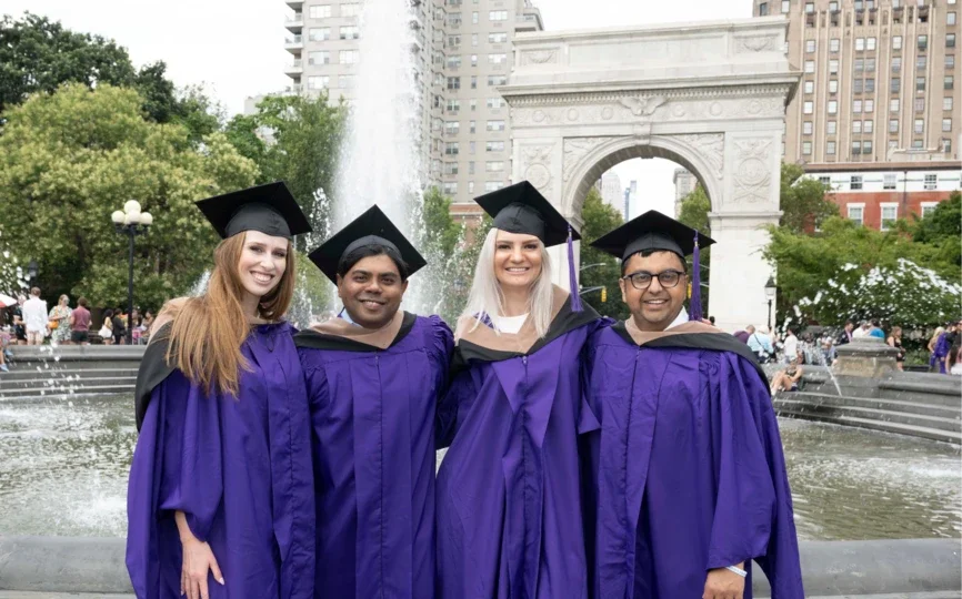 Four Stern students standing in front of the fountain in Washington Square Park with their violet graduation attire on. 
