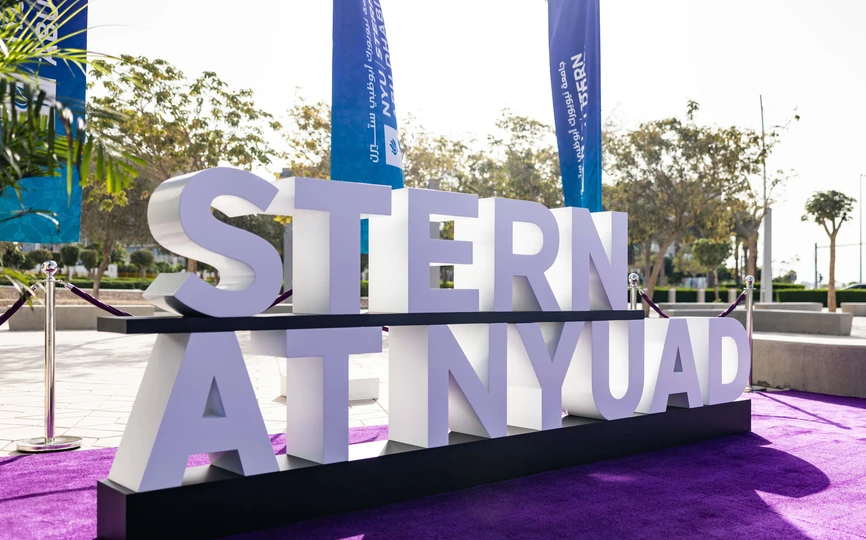 Stern at NYUAD sign with flags in the background