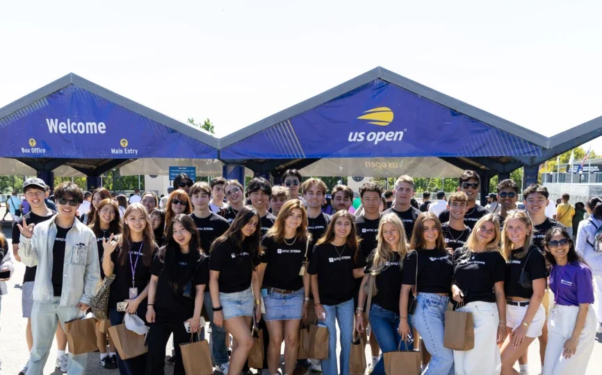 Students wearing NYU Stern shirts stand in front of US Open sign
