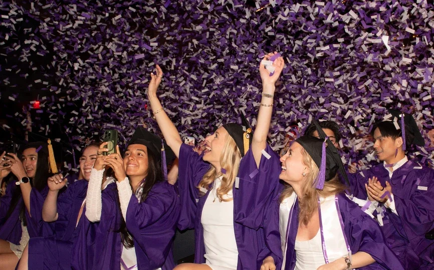 NYU Stern's Undergraduate students celebrating graduation as confetti falls down.