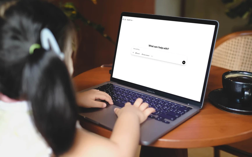 A young child at a laptop typing into ChatGPT