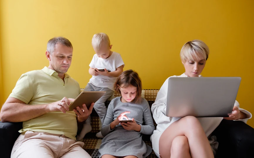 A family sitting together on a couch. Each person is looking at a smartphone, computer or electronic notebook