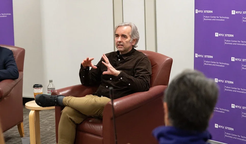 Dickerson sits in a chair and speaks to attendees