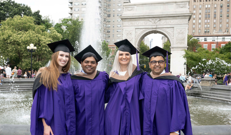 Four Stern students standing in front of the fountain in Washington Square Park with their violet graduation attire on. 