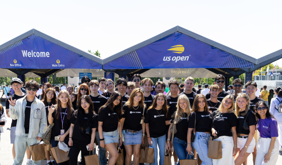 Students wearing NYU Stern shirts stand in front of US Open sign