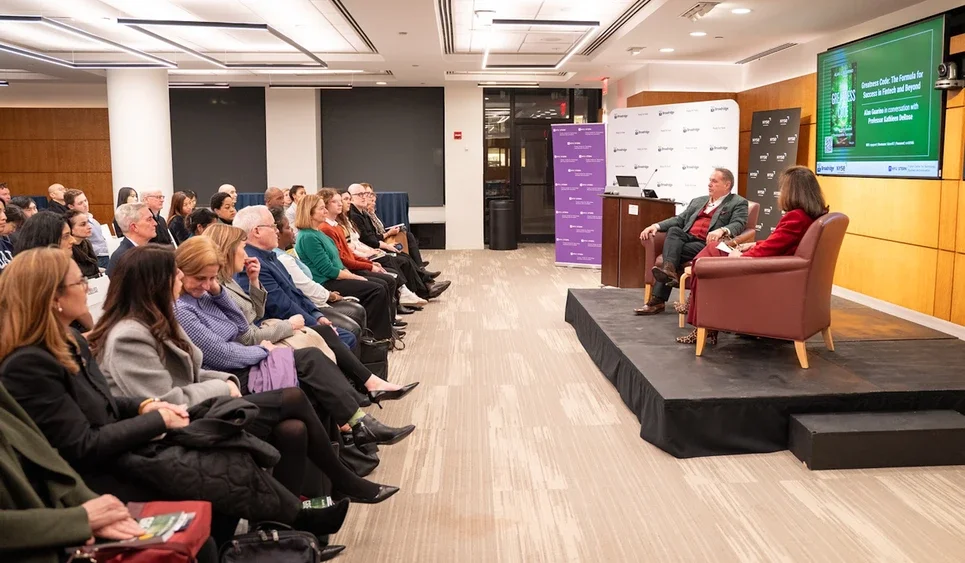 audience sits and watches the two speakers on a small platform