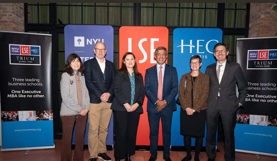 Six members of TRIUM leadership stand in front of banners with the TRIUM logo and logos from NYU Stern, LSE and HEC