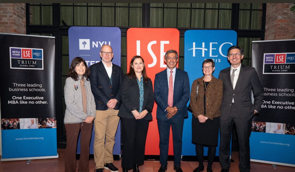 Six members of TRIUM leadership stand in front of banners with the TRIUM logo and logos from NYU Stern, LSE and HEC