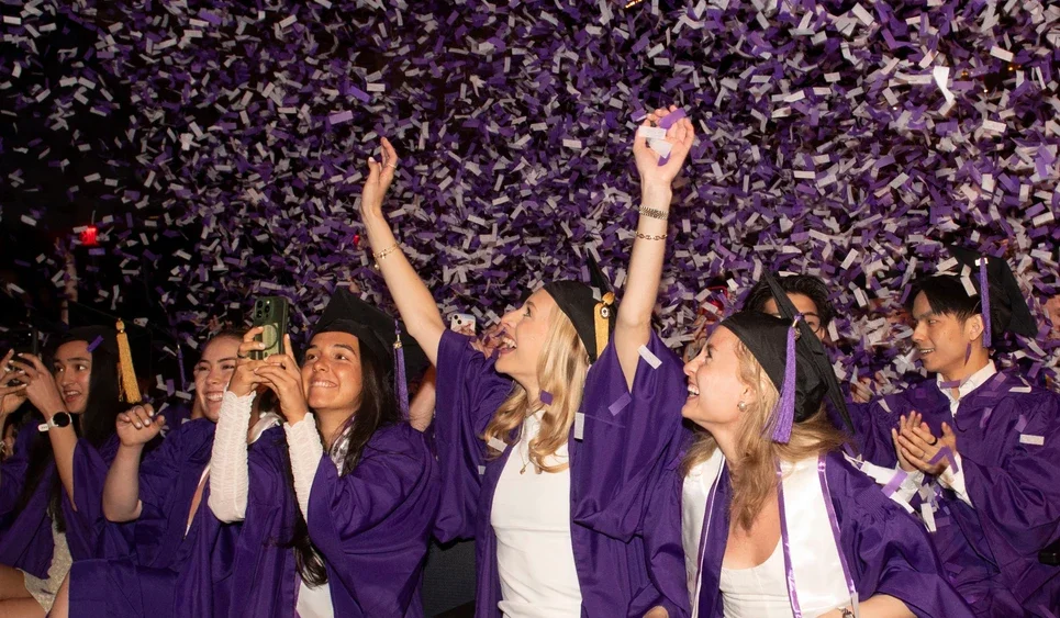 NYU Stern's Undergraduate students celebrating graduation as confetti falls down.