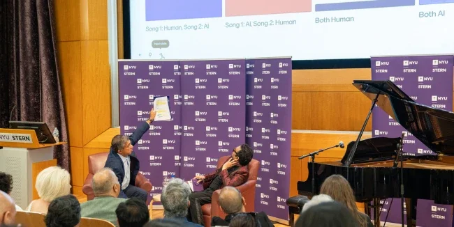 Dean Anand using a piece of paper to point to a screen in front of an audience