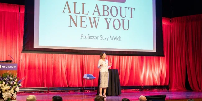 Professor Suzy Welch stands on a stage presenting to a crowd of MBA students
